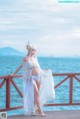 A woman in a white dress standing on a pier by the water.